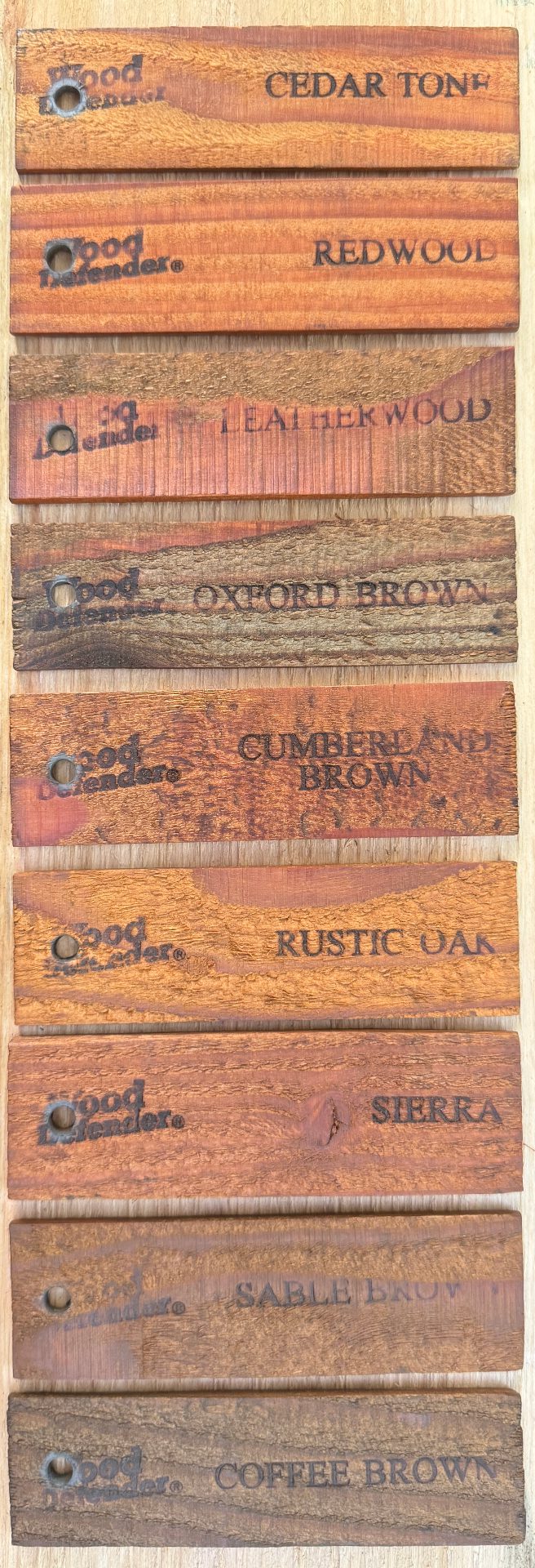 longpic Ten wooden planks display different wood stains, each labeled with its respective name: Cedar Tone, Redwood, Leatherwood, Oxford Brown, Cumberland Brown, Rustic Oak, Sierra, Sable Brown, Coffee Brown.