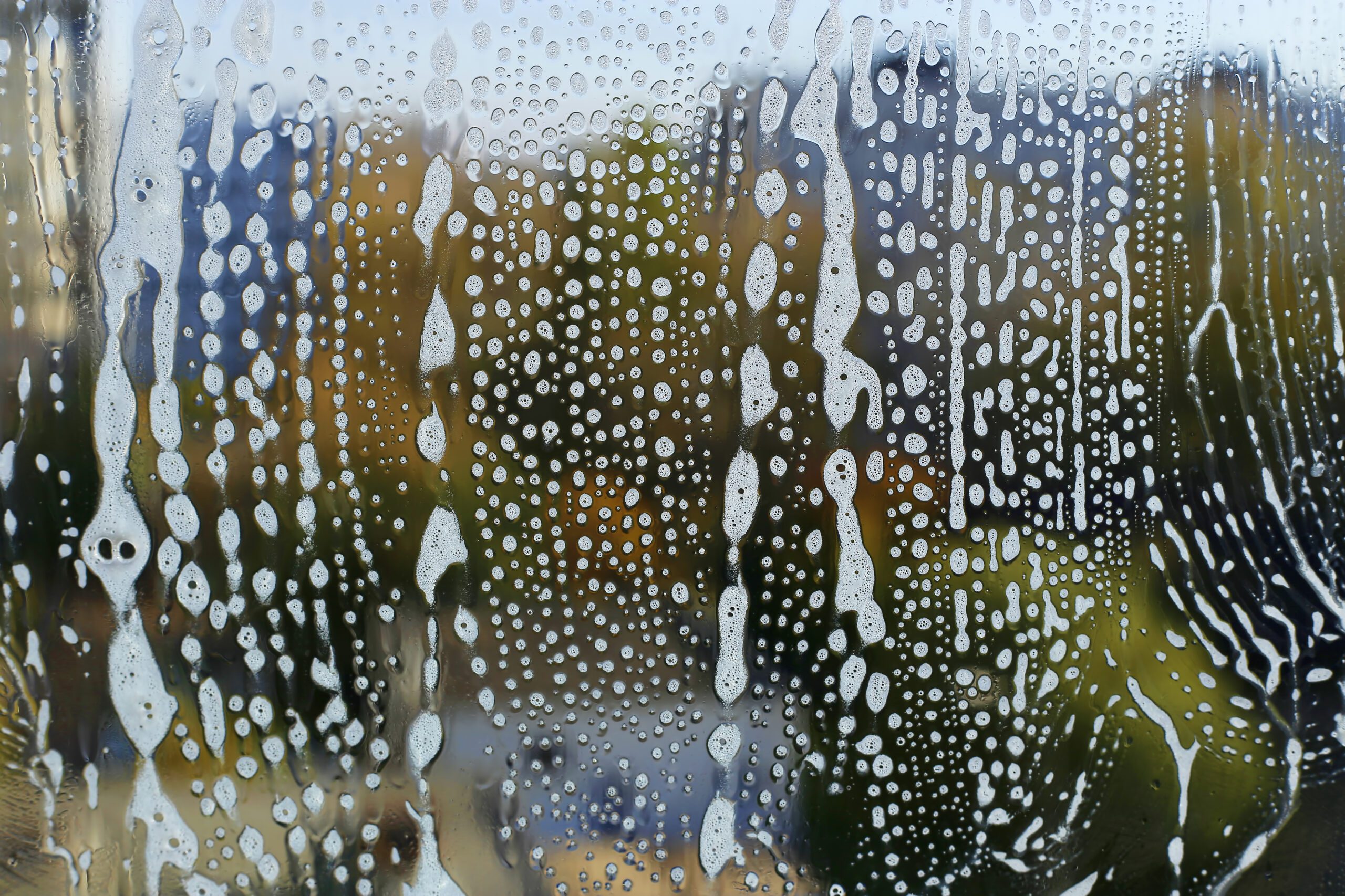 Natural texture with soap foam pattern on glass A close-up of a window covered in soap suds, with blurred outdoor scenery visible through the glass.